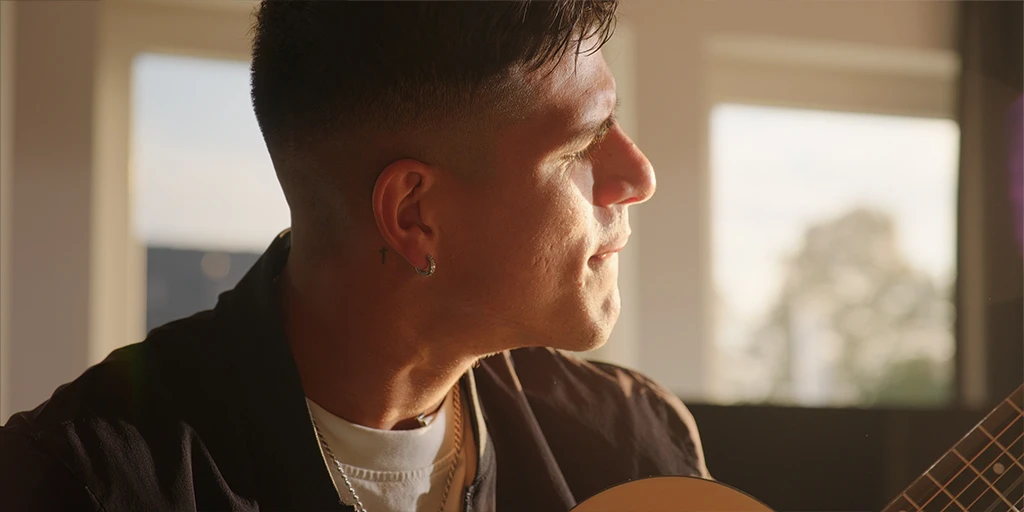 A young man (Piero Hincapié) plays guitar. Sunlight hits his face. He is in a villa.