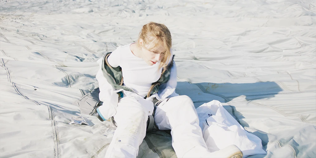 An astronaut (Odine Johne) sits on a white parachute. She struggles to peel off her spacesuit in the feature film »In the Sea of Silence«.