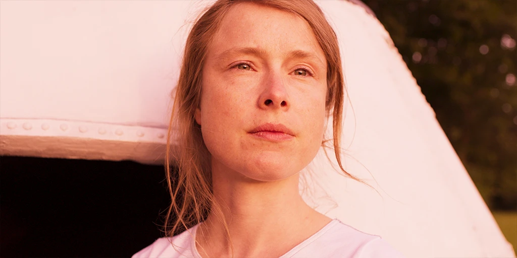 The protagonist of the film »The Mathematics of Things« transports a mattress over a railway crossing. The atmosphere is summery, the grass looks burnt.