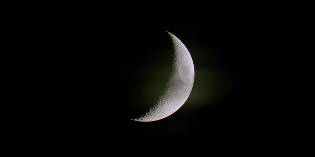 The moon is visible at night. About one-third of the depicted circular surface is illuminated by the sun. A veil of a cloud is visible in front of the moon. The structure of the moon is well recognizable in the feature film »In the Sea of Silence«.