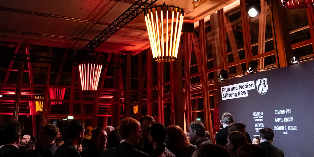 A hall illuminated in red, filled with people in evening attire.