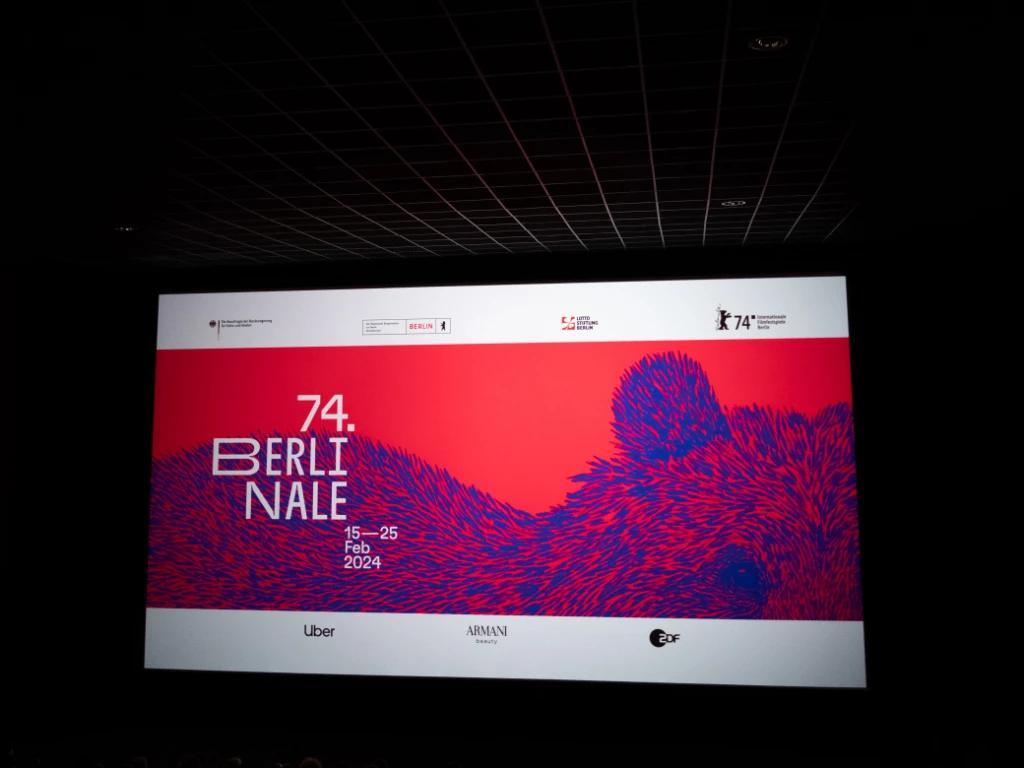 On the screen of a cinema, an intro screen shows a blue bear on a red background. Next to it is written '74. Berlinale'.