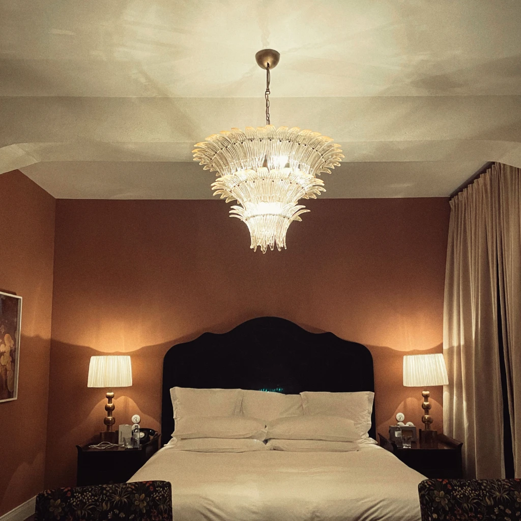 A bed in a chic hotel room with brown walls. In the foreground are two chairs.