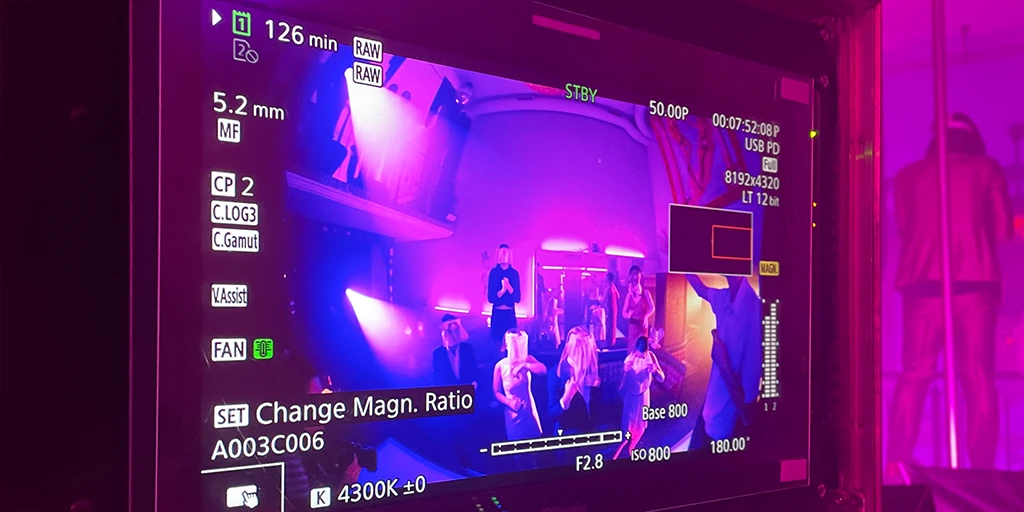 A monitor shows a bluish-magenta-lit strip club. Dancers are dancing on the tables.