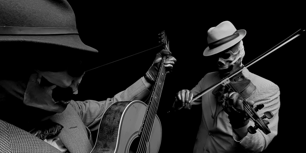 Very close on the left is a guitarist playing a piece on his guitar. He wears a dark hat and a skull mask. To his right, at a little more distance, stands a violinist. He plays his violin and also wears a skull mask and a light hat.