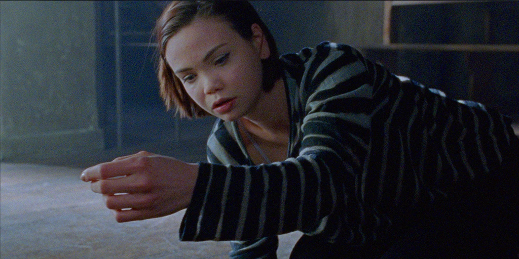 A young woman (Tatiana Feldman) sits on the chapel floor and looks at her arm.