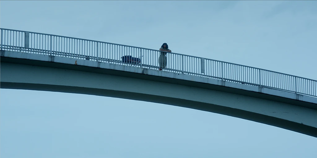 The protagonist of the film »The Mathematics of Things« stands on a bridge in a bluish atmosphere and looks at the landscape