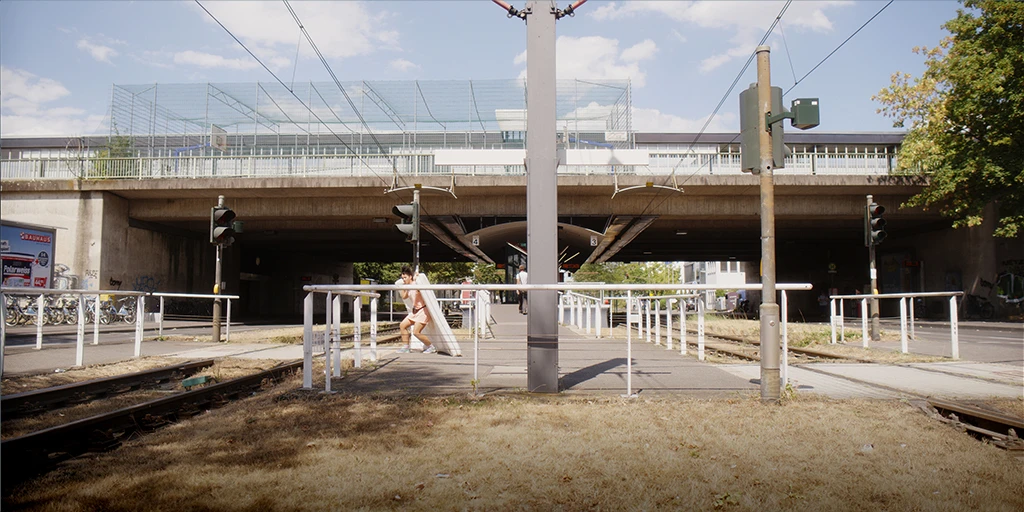 The protagonist of the film »The Mathematics of Things« transports a mattress across a railway crossing. The atmosphere is summery, the grass looks burnt.