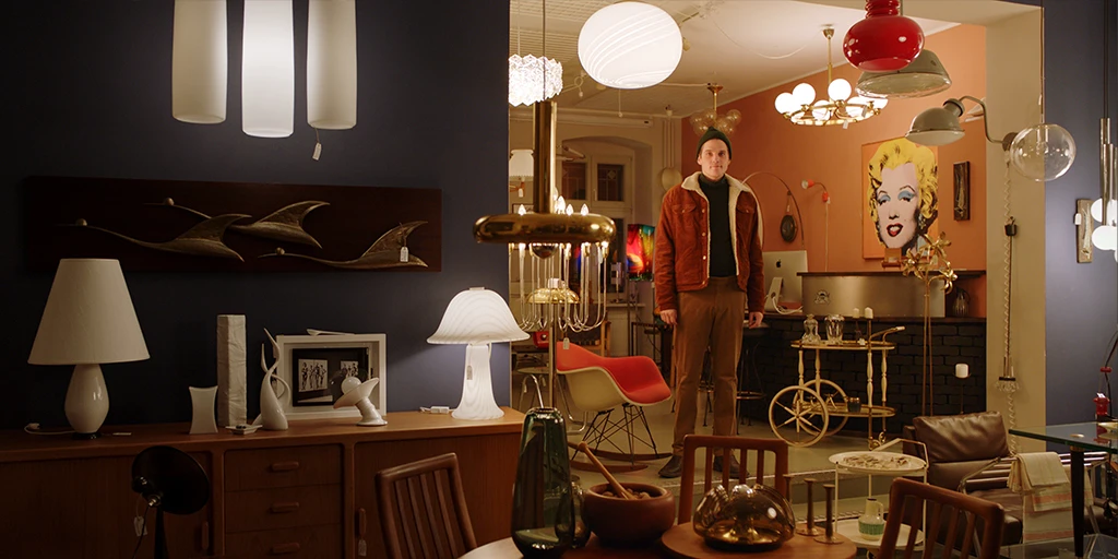 Louis (Benjamin Lillie) stands in a vintage furniture store and looks around. He looks alertly towards the camera in the TV commercial »True Romance«.